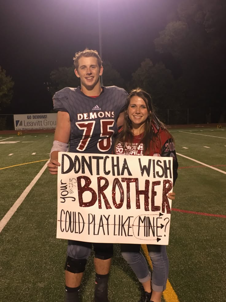 two people standing on a football field holding a sign that says, don'ttcha wish brother could play like mine?