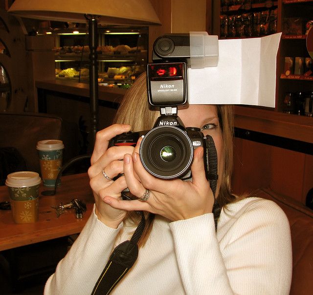 a woman holding up a camera to her face with a paper hat on it's head