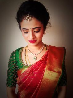 a woman wearing a red and green sari with gold jewelry on her neck, looking down