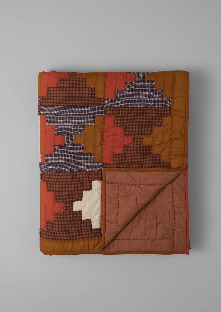 an orange and brown quilted blanket sitting on top of a white table next to a gray wall