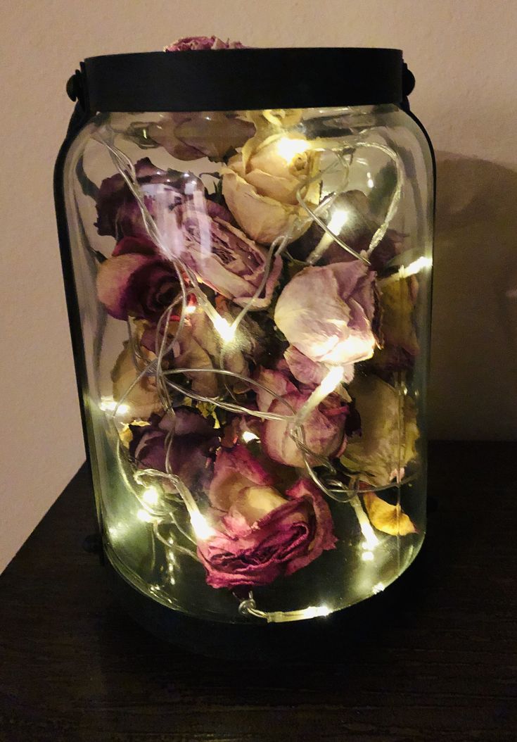 a glass jar filled with dried flowers on top of a wooden table next to a wall