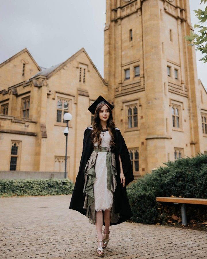 a woman in a graduation gown is walking towards a large building with a clock tower