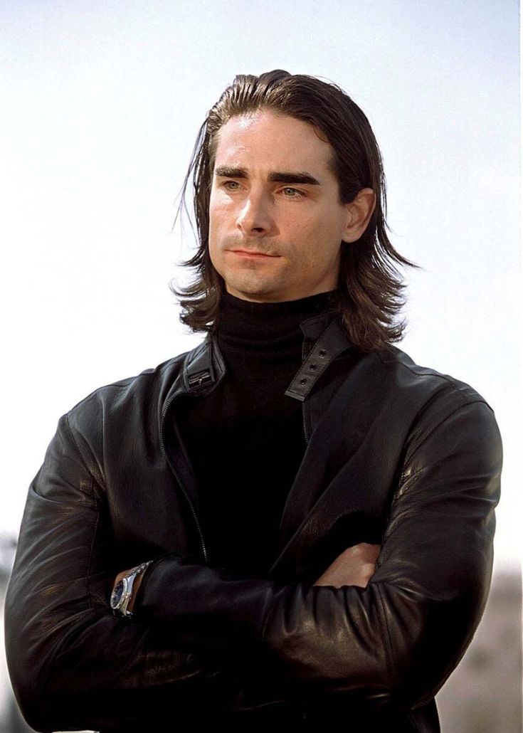 a man with long hair wearing a black turtle neck sweater and leather jacket looking at the camera