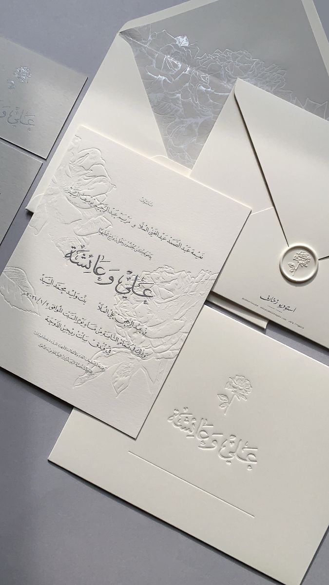 an elegant white wedding card with arabic writing on the front and back, set against a gray background