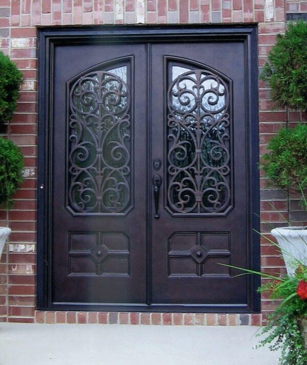 an ornate iron door with potted plants on the side and brick wall behind it