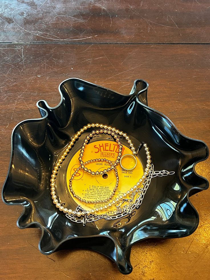 there is a black bowl on the table with some necklaces in it that says shell