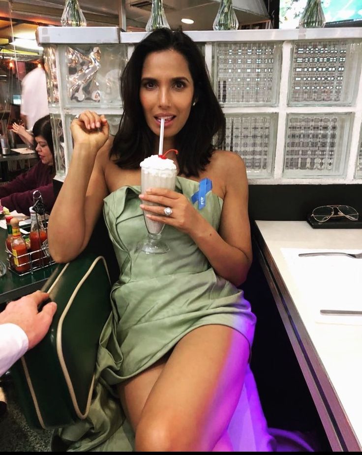 a woman in a green dress drinking from a straw cup while sitting at a table