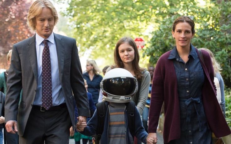 a man in a suit and tie walks with two children wearing an astronaut's helmet