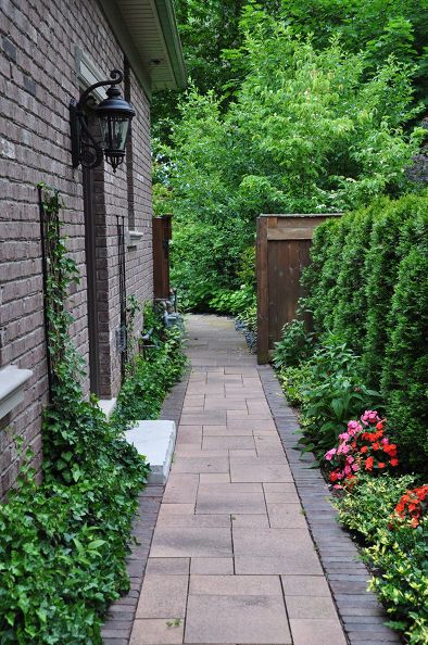 a brick walkway between two buildings surrounded by greenery and flowers in the foreground