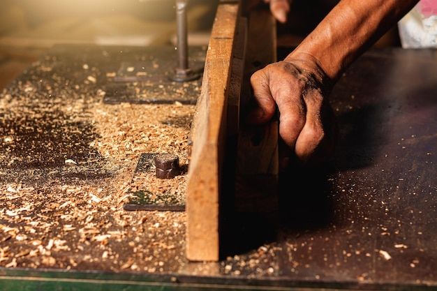 a man working with wood shavings on a piece of furniture in his workshop