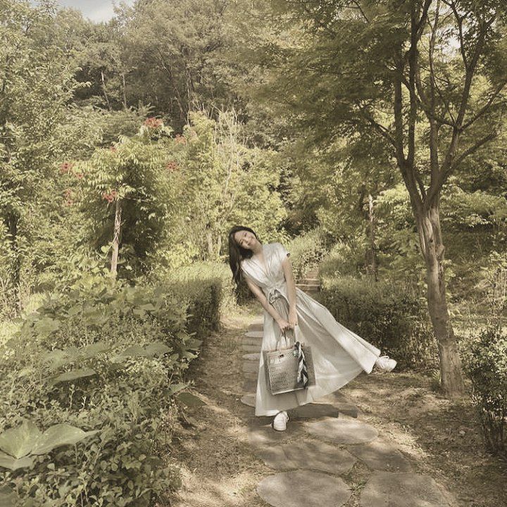 a woman is walking down a path in the woods with a handbag on her shoulder