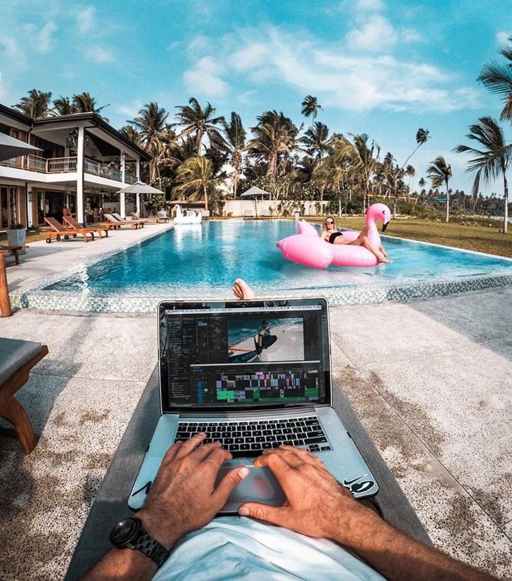 a man sitting in front of a laptop computer next to a pool