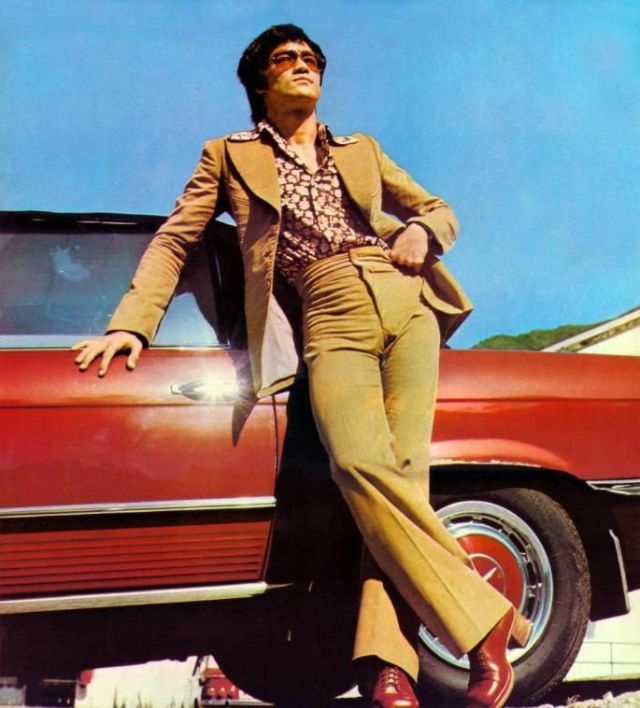 a man leaning on the side of a red car in front of a blue sky