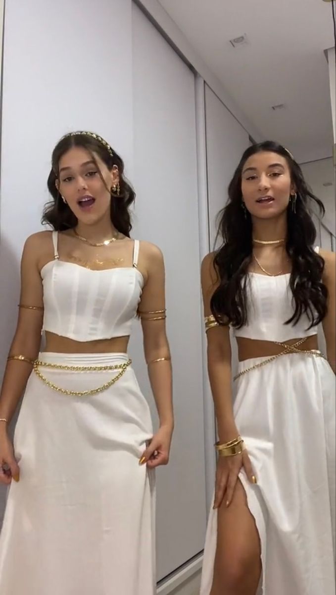 two women in white dresses standing next to each other with gold chains on their waist