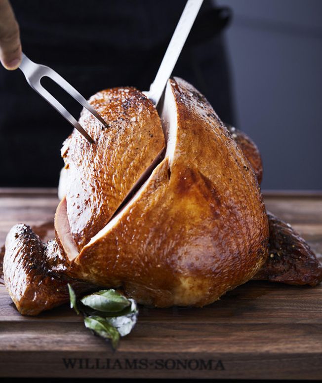 a roasting turkey on a wooden cutting board with tongs sticking out of it