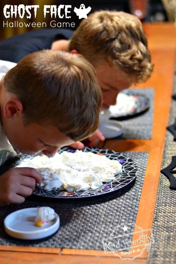 two young boys are eating cake together on the table with ghost face decorations around them