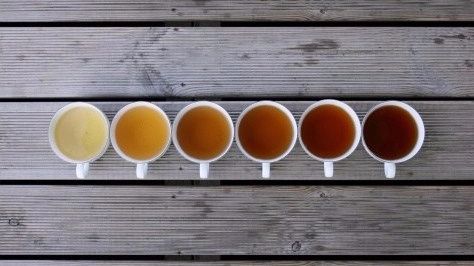 five different types of beer are lined up on a wooden planked surface, with one being filled with liquid and the other is empty