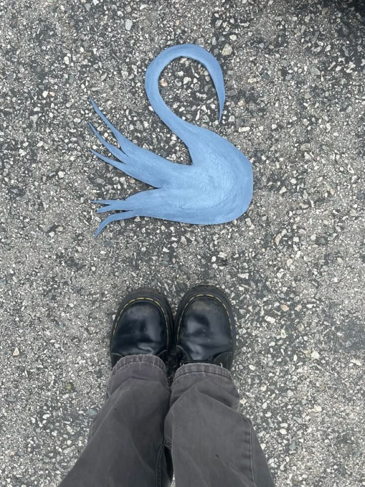 a person standing in front of a blue swan on the ground with their feet up