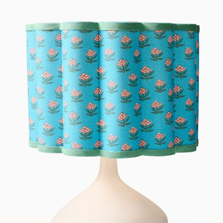 a blue lamp shade with pink flowers and green trim on a white base, in front of a white background