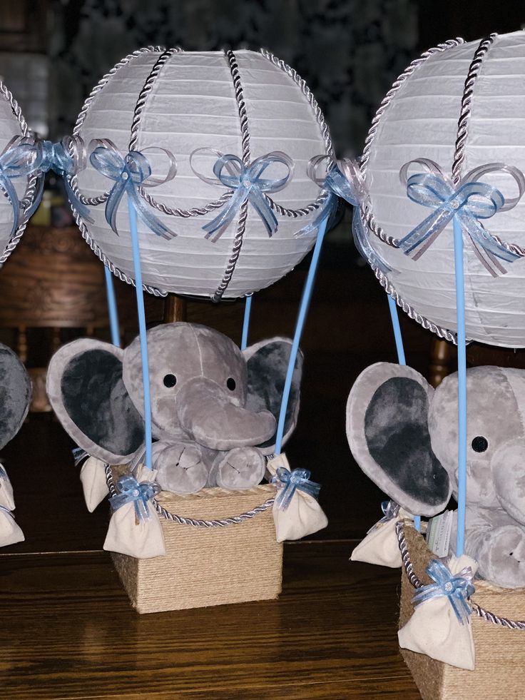 three stuffed elephants in small baskets with blue ribbons and paper lanterns attached to their heads