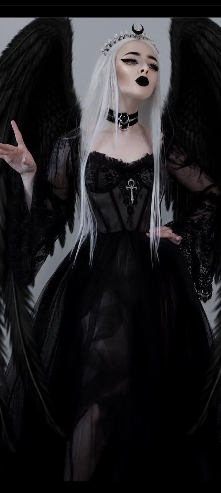 a woman with white hair and black makeup is dressed in gothic clothing, holding her hands out