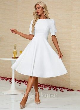 a woman in a short white dress standing next to a table with flowers on it