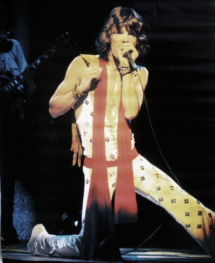 the man is performing on stage with his legs spread out and holding a microphone in one hand