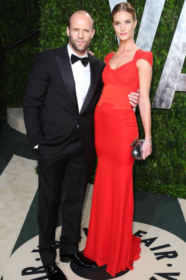 a man in a tuxedo and woman in a red dress posing for the camera