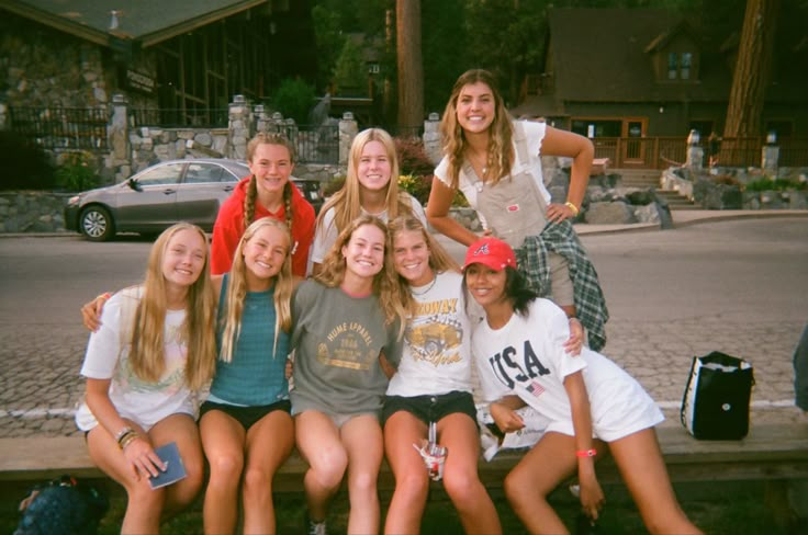 a group of young women sitting next to each other on top of a wooden bench