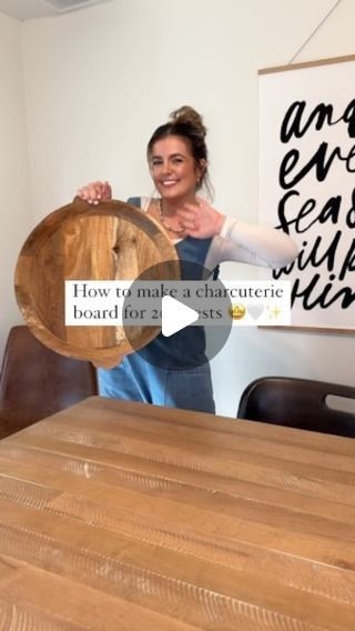 a woman holding a wooden plate in front of a table