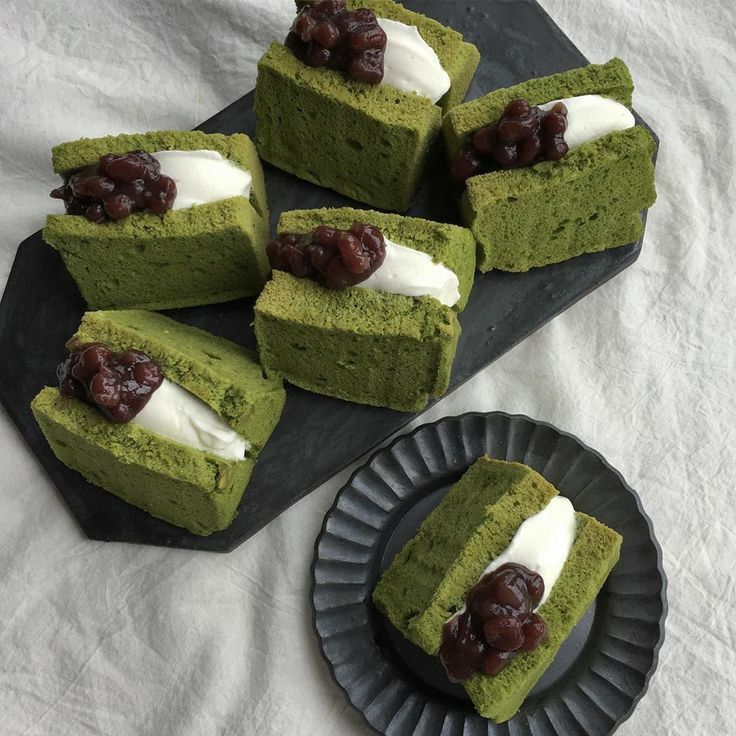 four pieces of green cake with white cream and cherries on top sitting on a black plate