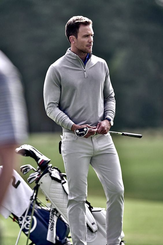 a man standing next to a golf bag on top of a grass covered field holding a golf club