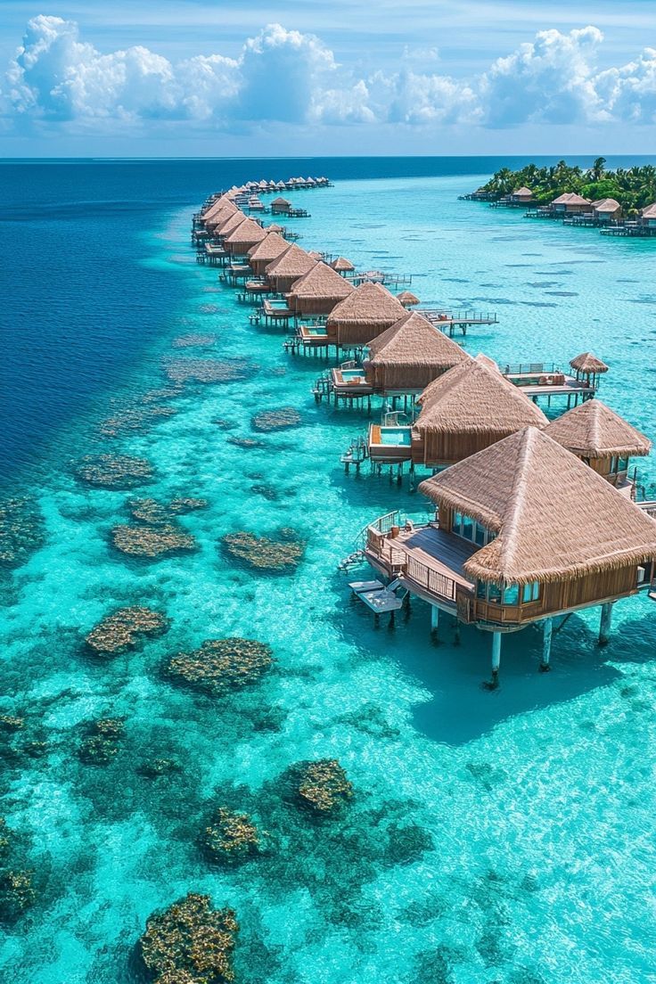 an aerial view of several overwater huts in the ocean with corals and blue water