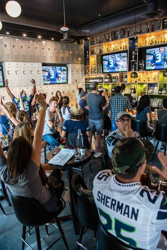 a group of people sitting at tables in a bar watching tvs and drinking beer