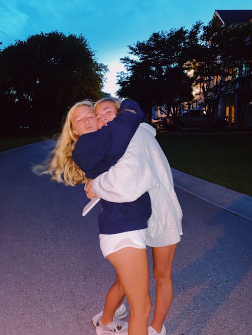 two women hugging each other on the street at night time with trees in the background