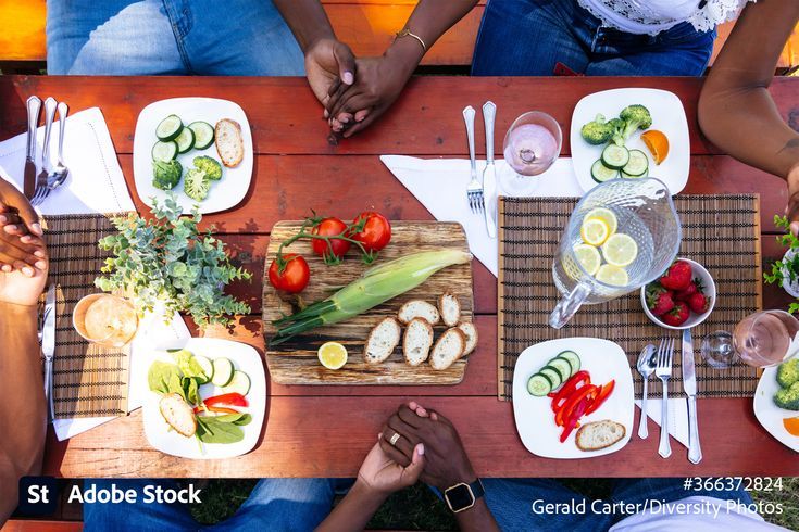 several people sitting at a table with plates of food and drinks on it, top view