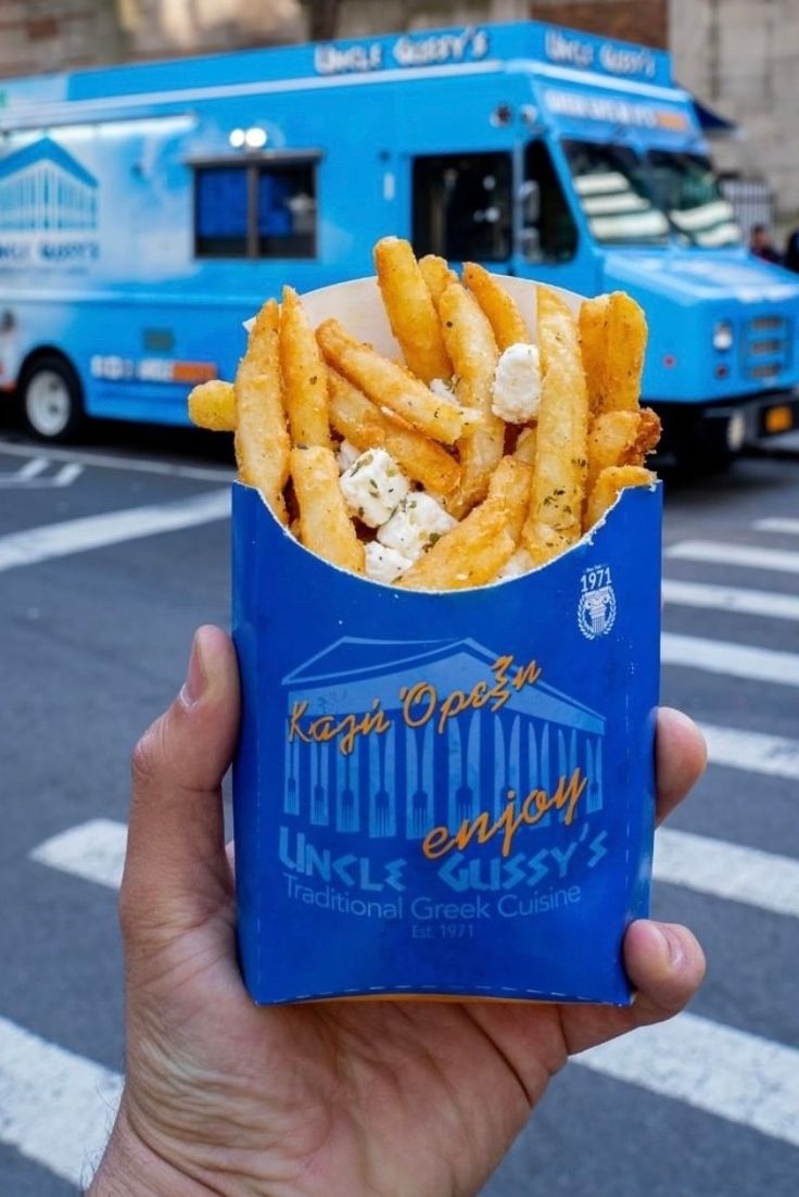 a person holding up a box of french fries in front of a blue food truck