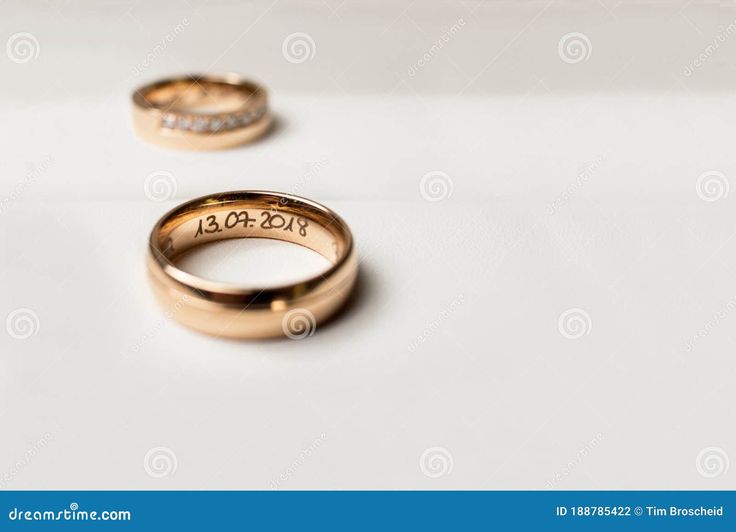 two gold wedding rings with the date on them and diamonds in front of each other