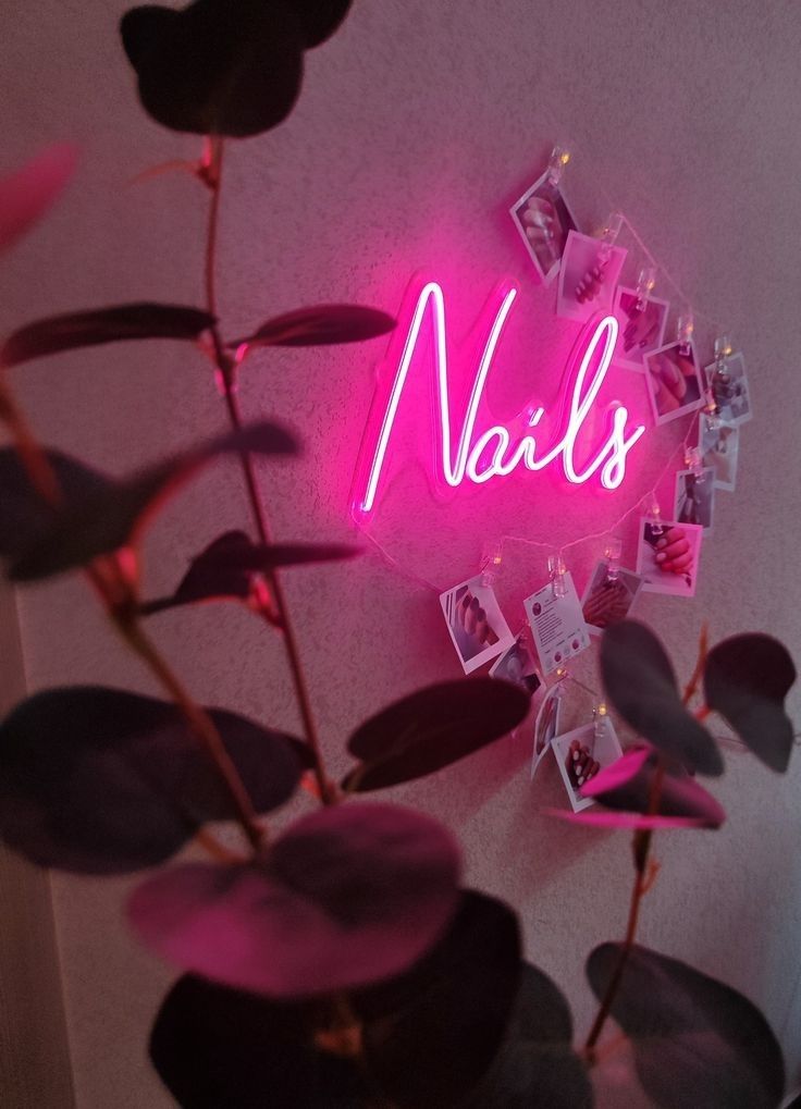 a pink neon sign that says nails on it next to a potted plant with leaves