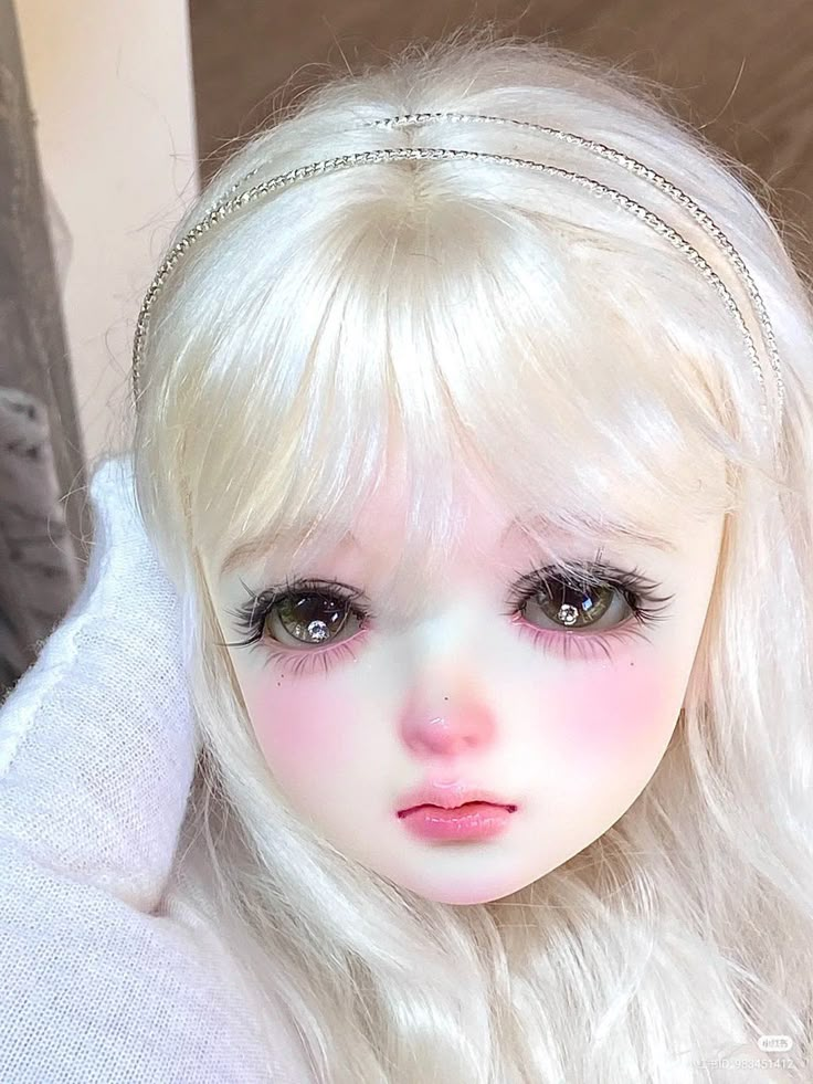 a close up of a doll with blonde hair and blue eyes wearing a headband