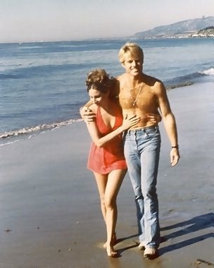 a man and woman walking on the beach next to the ocean with their arms around each other