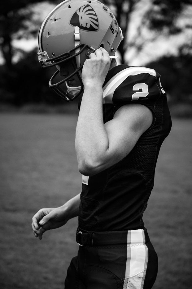 a young man in a football uniform is holding his helmet up to his face while standing on the field