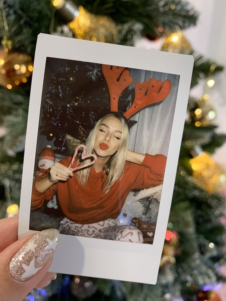 a woman holding up a polaroid photo in front of a christmas tree