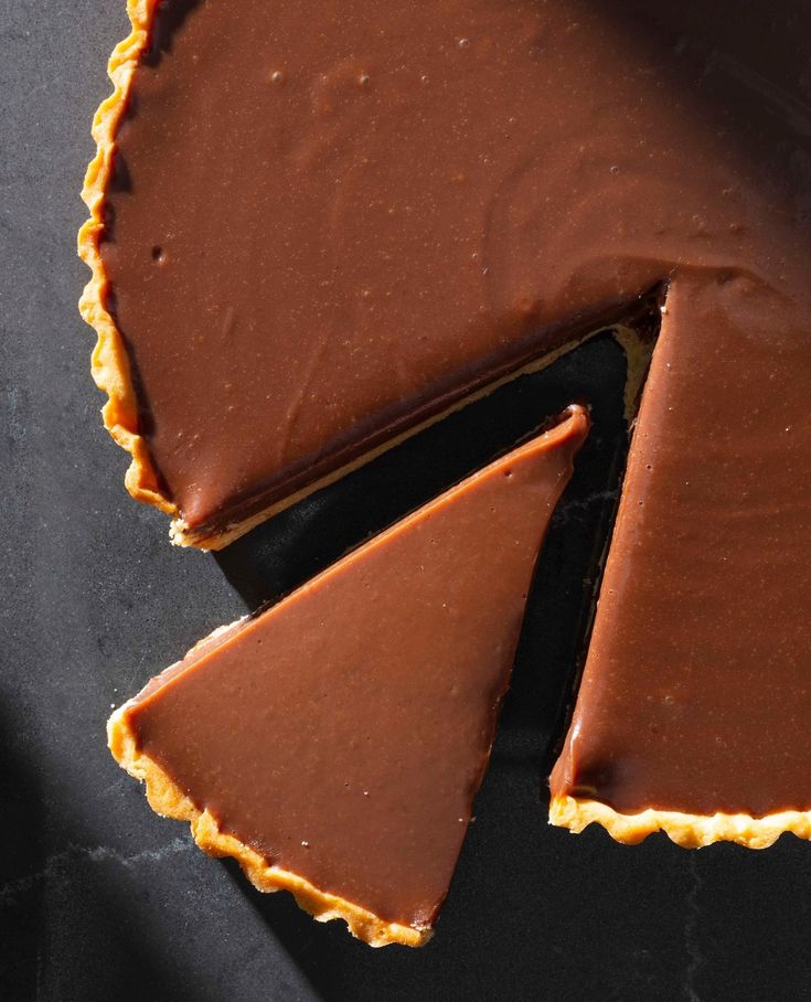 a chocolate tart with one slice cut out and the other half eaten, on a black surface