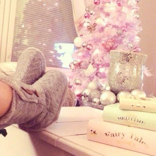 a woman laying on top of a bed next to a pink christmas tree and books