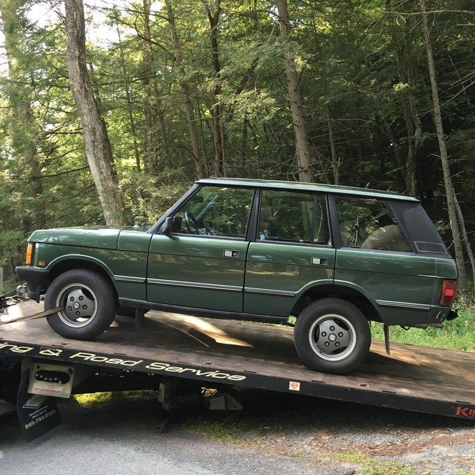 a green car is on the back of a flatbed tow truck with trees in the background