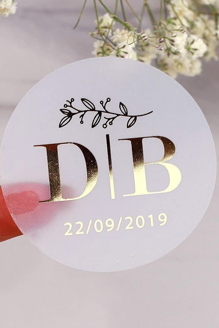 a white disc with gold lettering on it next to some flowers and red ribbon that says dib