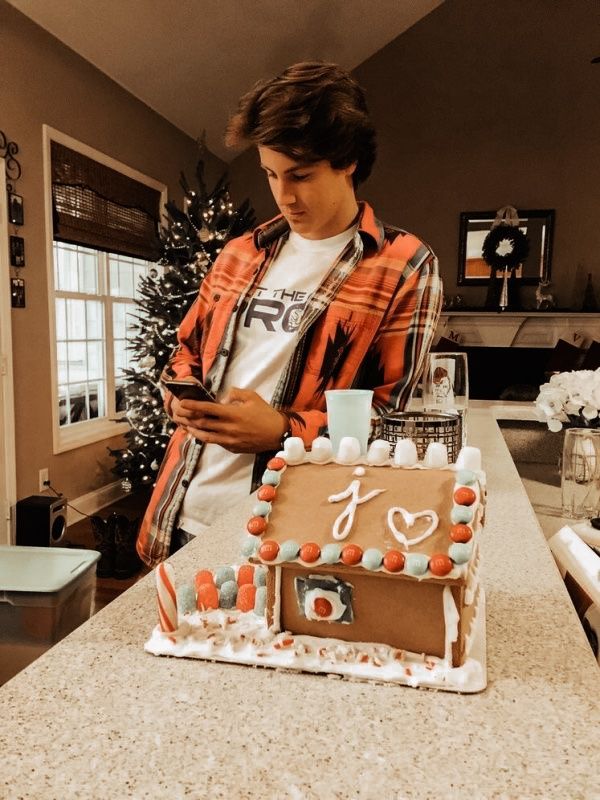 a young man standing in front of a gingerbread house made to look like he is looking at his cell phone