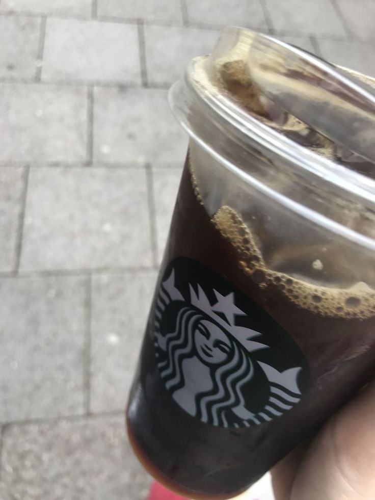 a person holding up a starbucks drink in their hand on the sidewalk with brick pavers