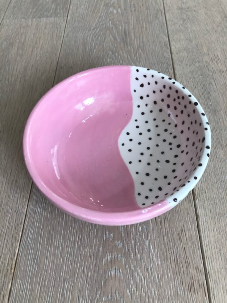 a pink and white bowl with black dots on it sitting on a wooden floor next to a wall